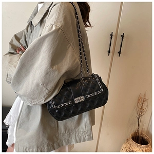 Detail of black quilted shoulder bag featuring silver chain strap and metal buckle closure