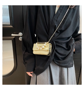 Détail du mini sac doré à chaîne avec texture crocodile et poignée élégante en perles