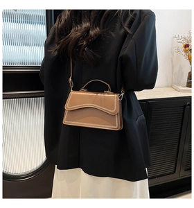 Detailed view of a brown leather crossbody bag with cream woven edges and metallic clasps