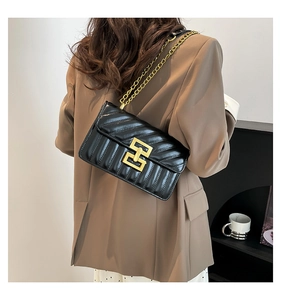 Detail view of a black quilted shoulder bag with gold chain strap and interlocking metal clasp