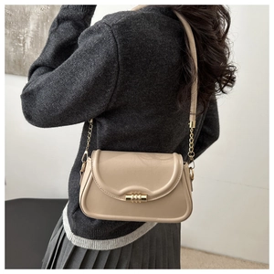 Detail of minimalist beige shoulder bag with gold clasp and chain strap on a model