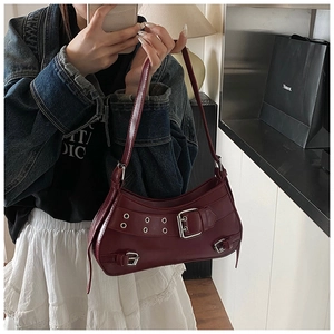 Close-up of burgundy underarm bag with silver buckles, eyelet studs, and zipper detail