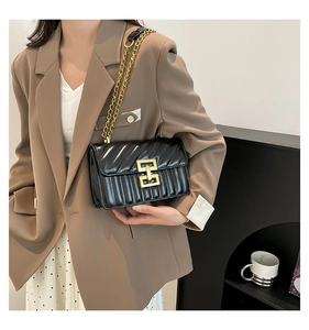 Chic black quilted shoulder bag with gold geometric lock worn over a tan blazer