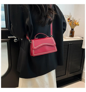 Detail of red glossy leather square bag featuring wavy edges and white stitching accents
