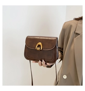 Detail of vintage brown leather saddle bag with gold U-shaped buckle and textured finish