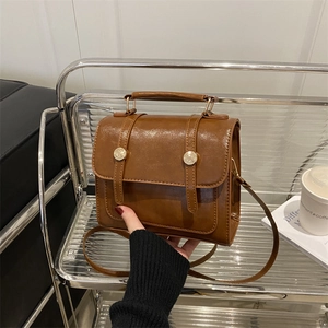 Brown vintage leather handbag with flap and metal buckles on a modern display shelf