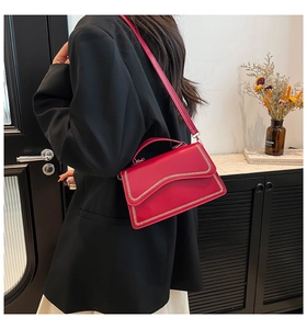 Detail of red leather square handbag with decorative gold wavy stitching and top handle