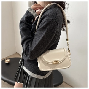 Close-up of beige shoulder bag with gold cylindrical metal lock and smooth faux leather texture