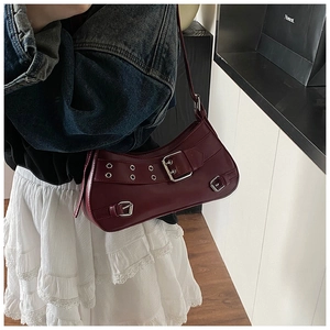 Detail of burgundy leather crescent shoulder bag with silver metallic buckles and grommets