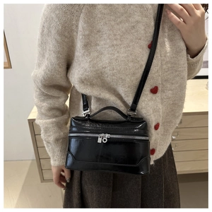 Detail of a black glossy box bag with silver zipper and adjustable shoulder strap