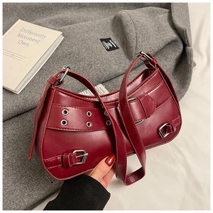 Macro detail of wine red leather handbag featuring buckle straps and metallic eyelets