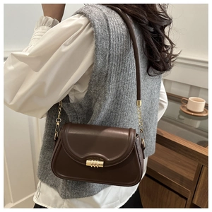 Detail of dark brown leather underarm bag with gold cylindrical lock and chain strap
