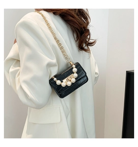 Détail du mini sac noir texture crocodile avec poignée en perles sur costume blanc