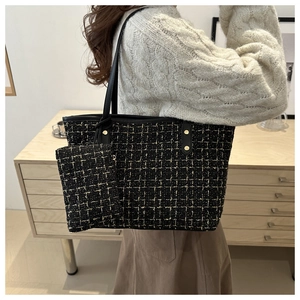 Detail view of a black tweed tote bag with metal rivets and matching mini pouch on a model