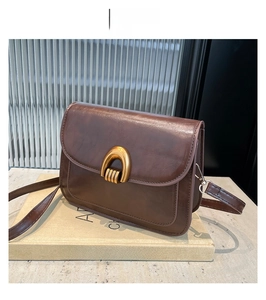 Detail of coffee brown vintage crossbody bag with gold U-shaped metal buckle on a book
