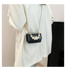 Détail du sac noir motif crocodile avec poignée en perles et chaîne dorée sur veste