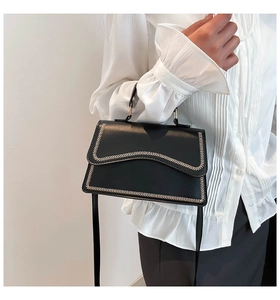 Detail of black wave flap handbag with contrast stitching on white shirt background