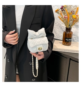 Detail der weißen gesteppten Mini-Tasche mit Schleife und goldener Kette am Model