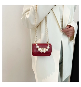 Close-up of burgundy croc-effect bag featuring elegant pearl decor and golden chain strap