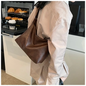 Gros plan d'un grand sac cabas marron foncé porté par un mannequin dans un café douillet
