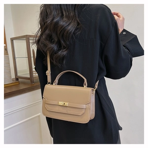 Close-up of khaki leather handbag with gold metal clasp shown on model for size reference