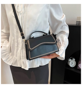 Detail of black leather square handbag with golden V-shaped trim and adjustable strap