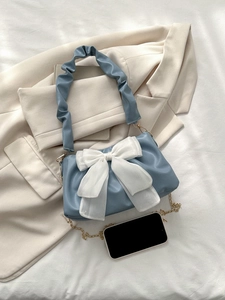 Detail of blue pleated shoulder bag featuring a large white bow and metal chain strap