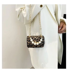 Détail du mini sac léopard avec chaîne dorée et poignée en perles sur un costume blanc