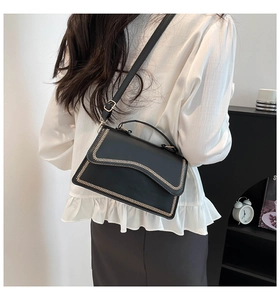 Detail of elegant black crossbody bag with gold woven trim shown on a model's back
