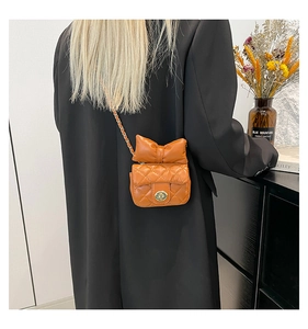 Detail van felle oranje gewatteerde crossbodytas met grote strik en gouden slot