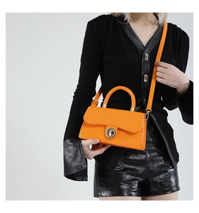 Petit sac carré orange vif avec boucle dorée ronde porté sur une tenue noire