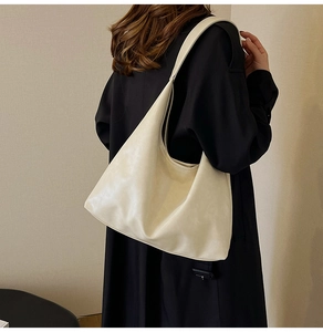 Détail du sac hobo en cuir crème porté par un mannequin en trench-coat sombre