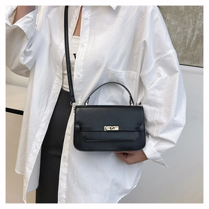 Detail of minimalist black leather handbag featuring a golden rectangular twist lock