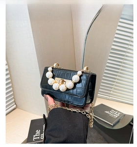 Détail d'un mini sac noir texture crocodile avec poignée perle et chaîne dorée