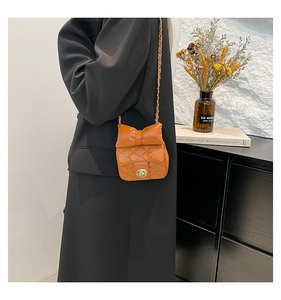 Detail of caramel orange quilted mini bag featuring a bow design and gold chain strap