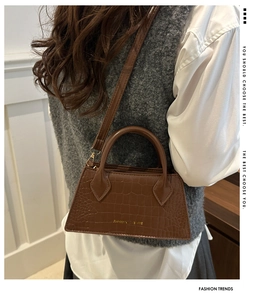 Detail of dark brown crocodile texture leather handbag worn by model in a casual setting