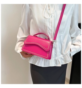 Detail of fuchsia square handbag featuring golden chain stitching and top handle