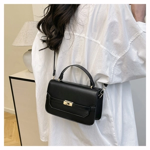 Détail d'un sac à bandoulière noir avec fermoir doré porté sur une chemise blanche