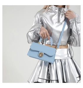 Sac carré bleu clair chic avec fermoir rotatif doré, porté par un mannequin en tenue stylée