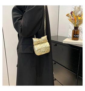 Macro shot of gold quilted crossbody bag featuring a bow accent and twist-lock buckle