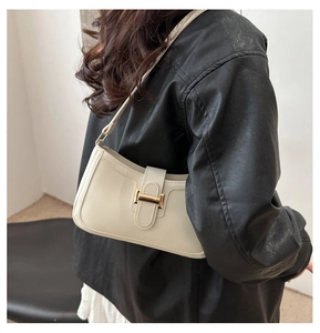 Détail du sac sous le bras crème avec boucle dorée porté sur une veste en cuir noir