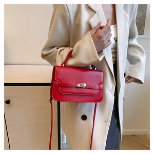 Detail of red leather crossbody bag with golden twist lock worn by a model