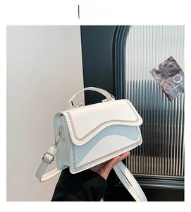 Detail of white leather handbag featuring wavy edges and brown V-shaped decorative stitching