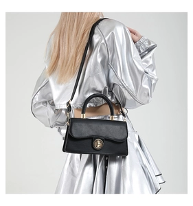 Sac à main carré noir avec boucle dorée porté par un mannequin en tenue argentée