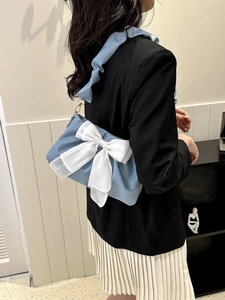 Close-up of a light blue shoulder bag featuring a large white bow and ruffled strap detail