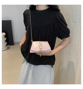 Pink patent leather crossbody bag with gold tassel logo shown on model with chain strap