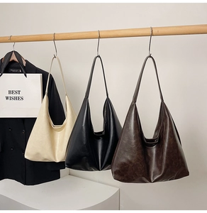 Three minimalist large hobo bags in beige, black and brown hanging on a wooden rack