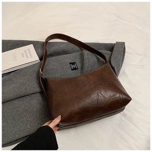Détail du sac hobo vintage en similicuir marron foncé texturé posé sur un manteau