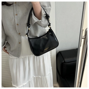 Detail view of black glossy underarm bag with gold knot hardware on shoulder strap