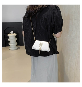 Detail view of a white crossbody bag with gold logo fringe and chain strap on a model